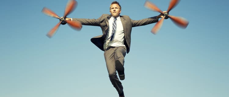 Businessman adventurer holds a set of spinning airplane propellers getting ready to fly in blue sky