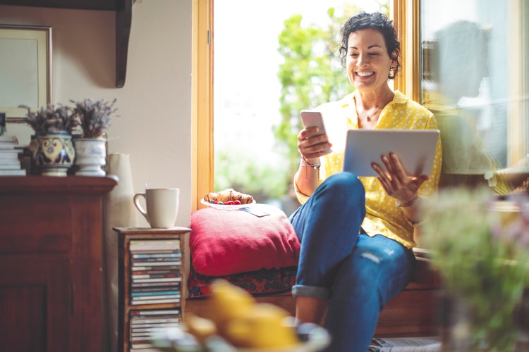 Mature woman is purchasing online, while seated at home with a laptop and a cellphone