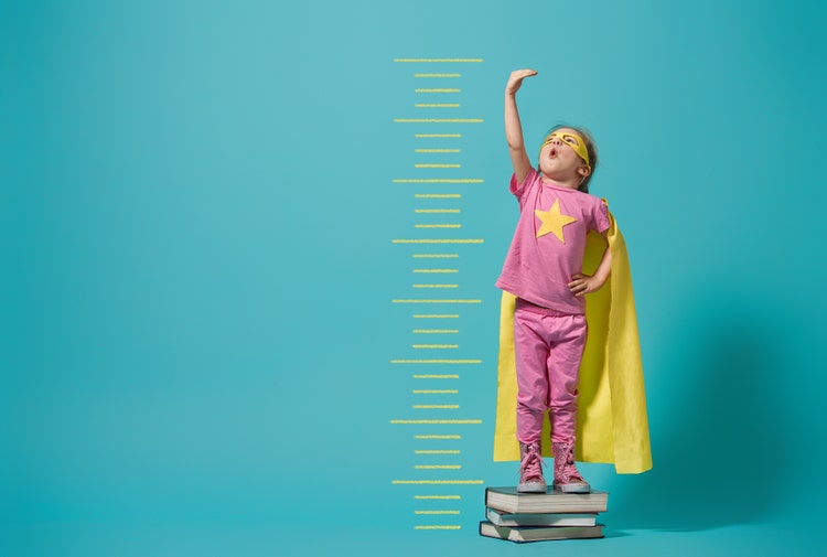 Little child playing superhero. Kid measures the growth on the background of bright blue wall. Girl power concept. Yellow, pink and turquoise colors.
