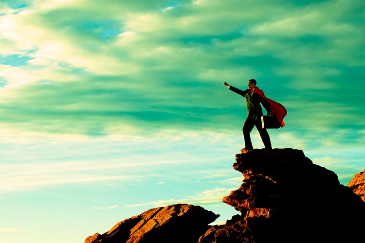 Business man in cape on top of mountain.