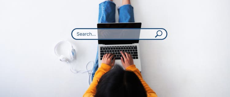 View from above of a woman sitting on a white floor typing into her laptop with a search bar superimposed over the top of the image.
