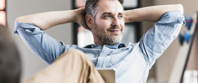 A man in business casual clothes reclines confidently with a laptop computer open on his lap.