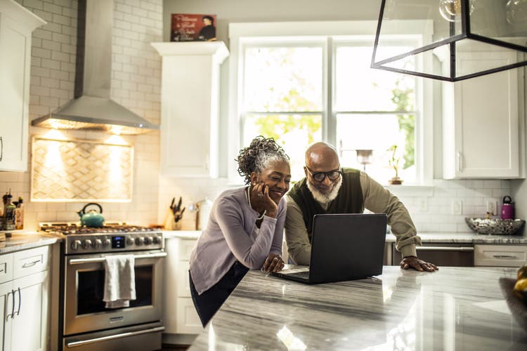 Senior couple using laptop in kitchen of suburban home