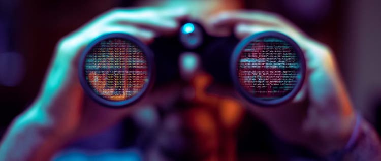 Man looking through binoculars with code reflected in the lenses.