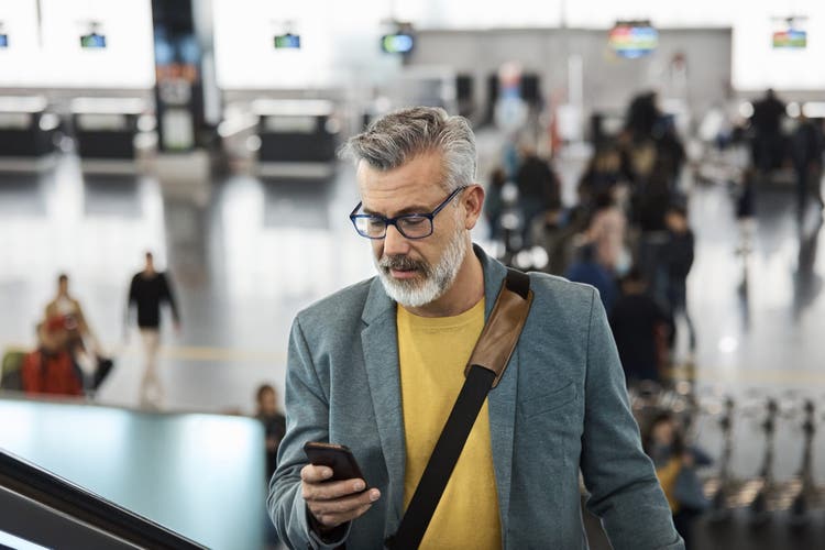 Male commuter using smart phone while standing on escalator. Mature man is holding mobile phone at railroad station. He is wearing blazer.