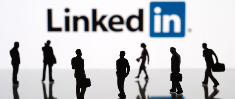 Human figurines standing in front of Apple iPad monitor displaying LinkedIn logo.