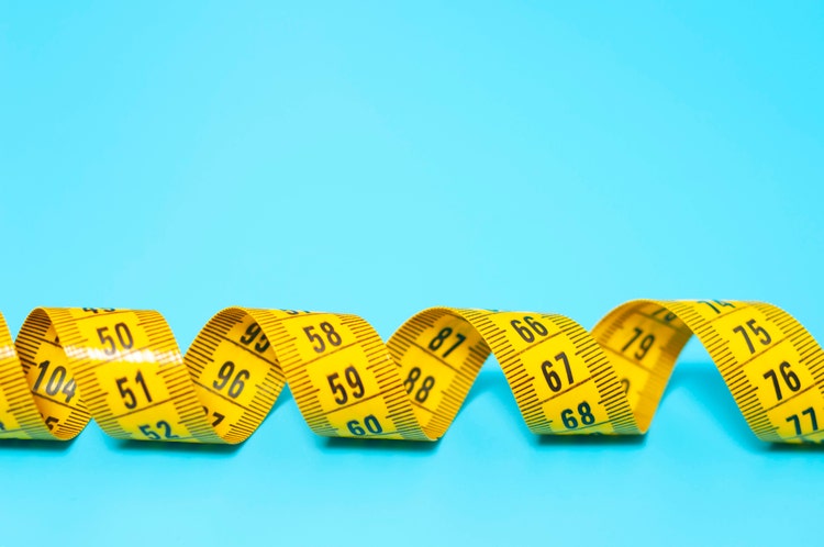 Yellow measuring tape on a blue background, copy space. The topic of weight loss, diet, proper nutrition, excess weight, tailoring.