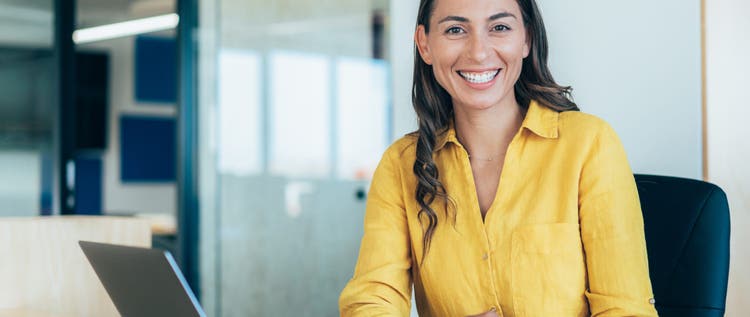 Confident businesswoman working on laptop at her workplace at modern office. Portrait of businesswoman in front of her laptop, looking at camera.