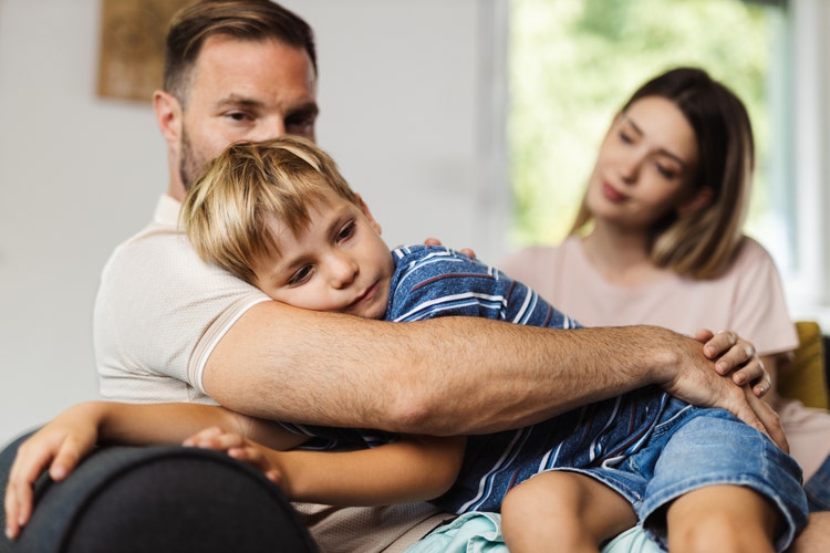 Young parents consoling their sad boy at home