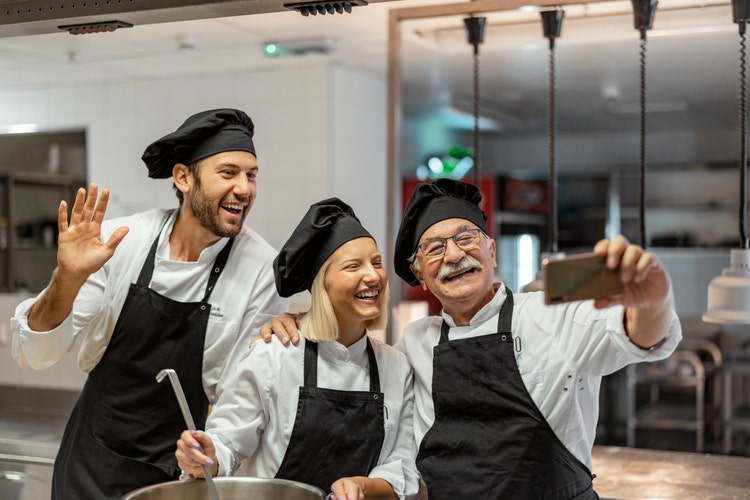 Senior male chef make selfie while working in a modern kitchen with his staff