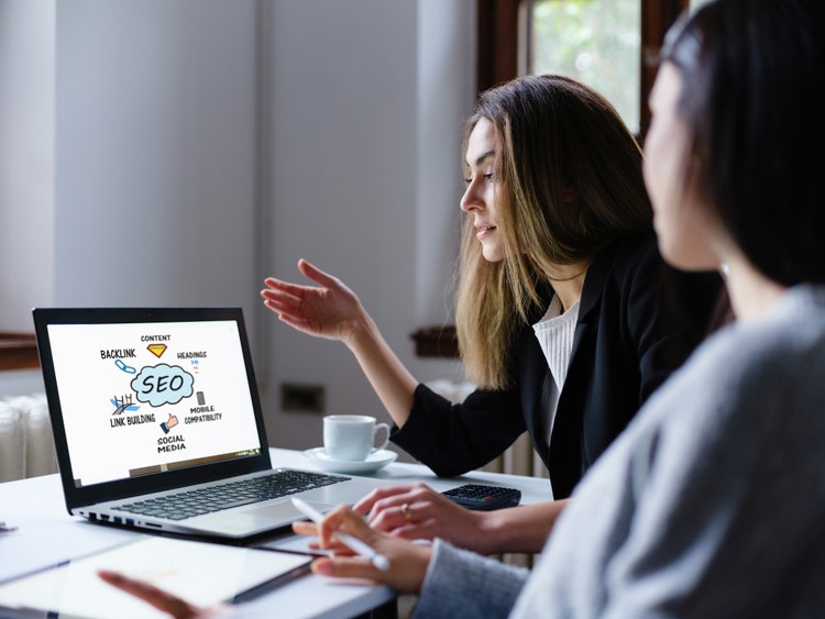 Search Engine Optimization (SEO) Concept On Computer Screen With Two Businesswomen In The Office