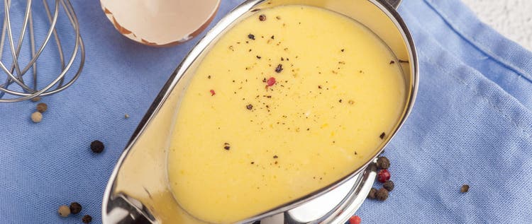 Hollandaise sauce. Classic French cuisine sauce. Emulsion sauce of butter and egg yolks with vinegar. Served in a gravy boat on a blue napkin. Close up and horizontal orientation.