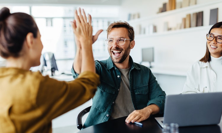 Successful business people giving each other a high five in a meeting. Two young business professionals celebrating teamwork in an office.
