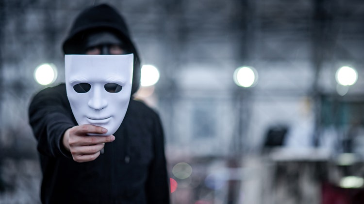 Mystery hoodie man with black mask holding white mask in his hand.