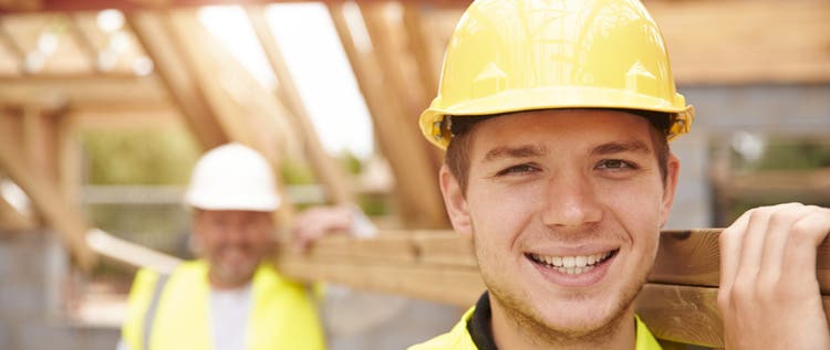 Builder And Apprentice Carrying Wood On Construction Site