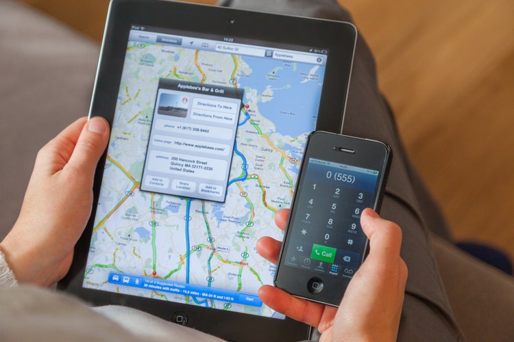 Female hand writing text message with iPhone 4 and other hand holding iPad 2 viewing google maps.