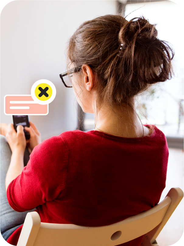 Person from behind in a chair, looking at a smartphone with an overlay icon showing a message bubble with an X, suggesting dismissing or deleting a message.