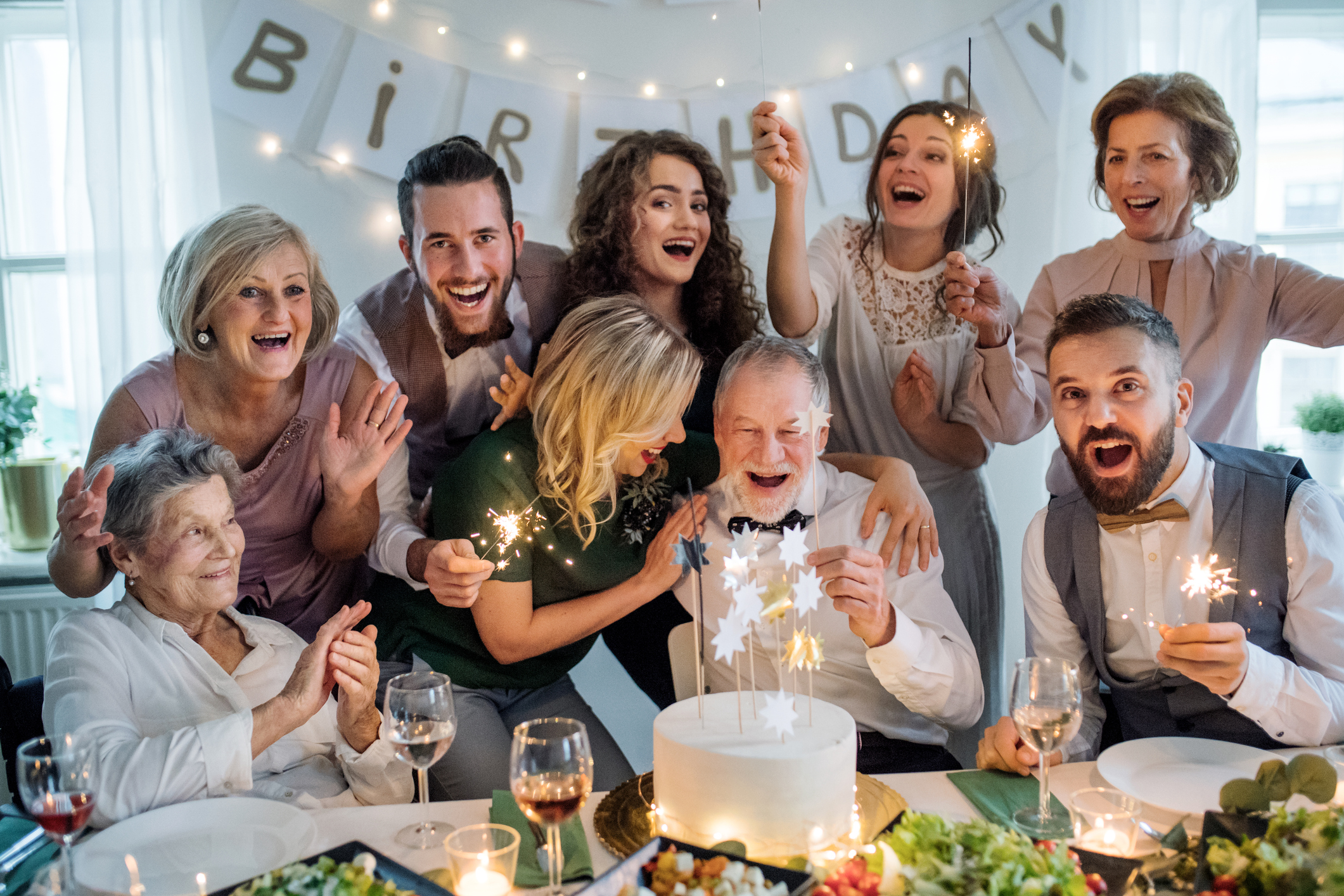 A senior man with multigeneration family and a cake celebrating birthday on an indoor party.