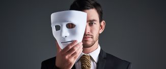 Studio portrait of a young businessman holding a mask in front of his face against a gray background