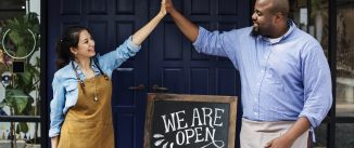 Cheerful business owners standing with open blackboard