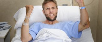 young angry patient man at hospital room lying in bed pressing nurse call button feeling nervous and upset in some kind of emergency health care and medical attention concept