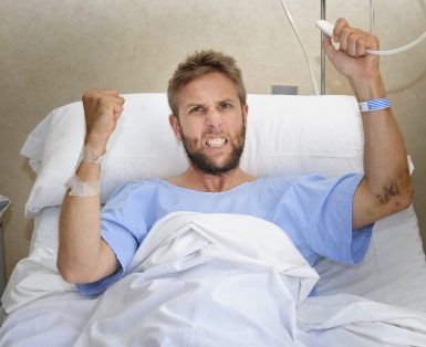 young angry patient man at hospital room lying in bed pressing nurse call button feeling nervous and upset in some kind of emergency health care and medical attention concept