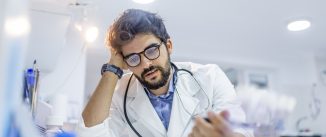 Overworked doctor in his office. Mid adult doctor contemplating in his office. Worried and tired mid adult male doctor reading medical results on his clipboard.