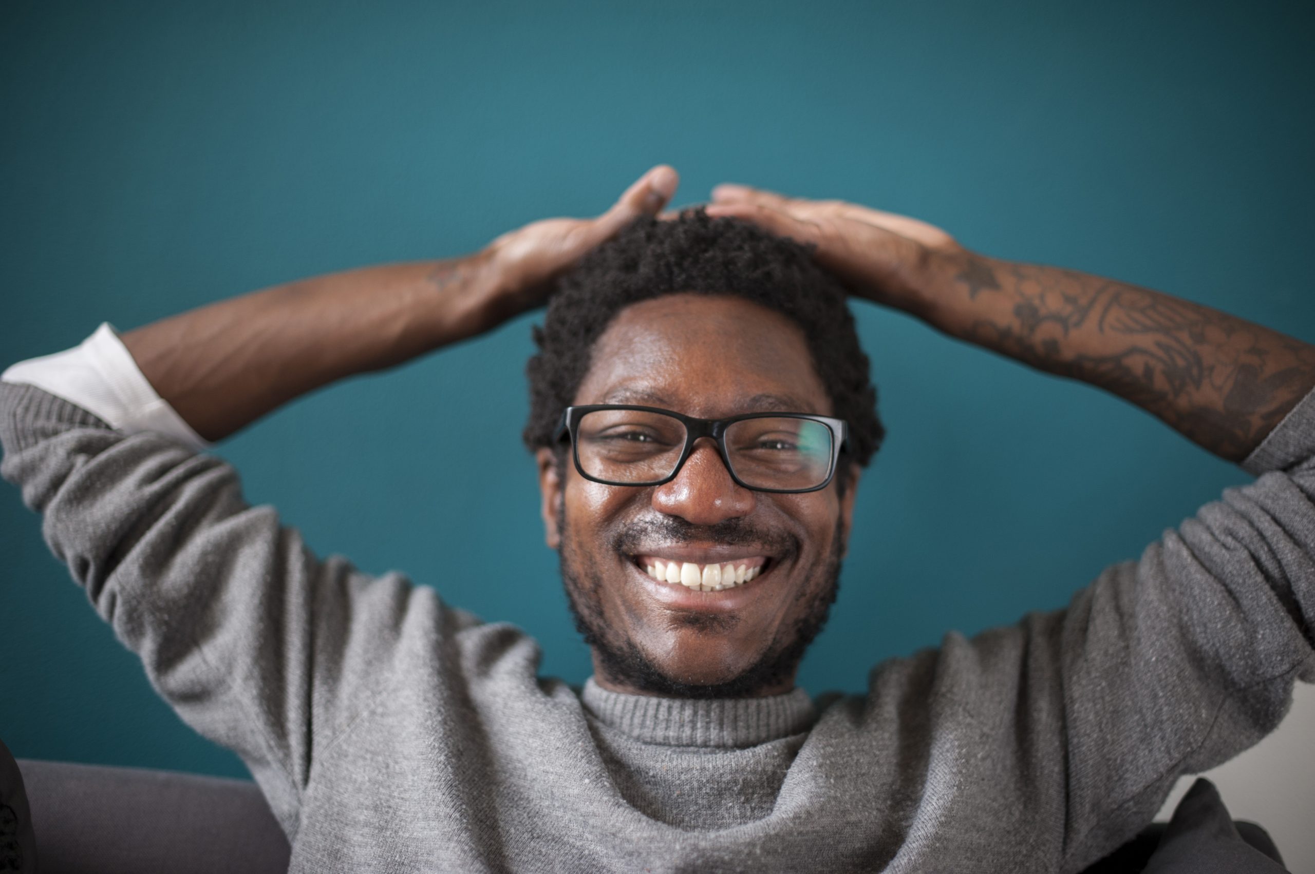 Man holding his arms behind his head, stretching and laughing a broad smile.