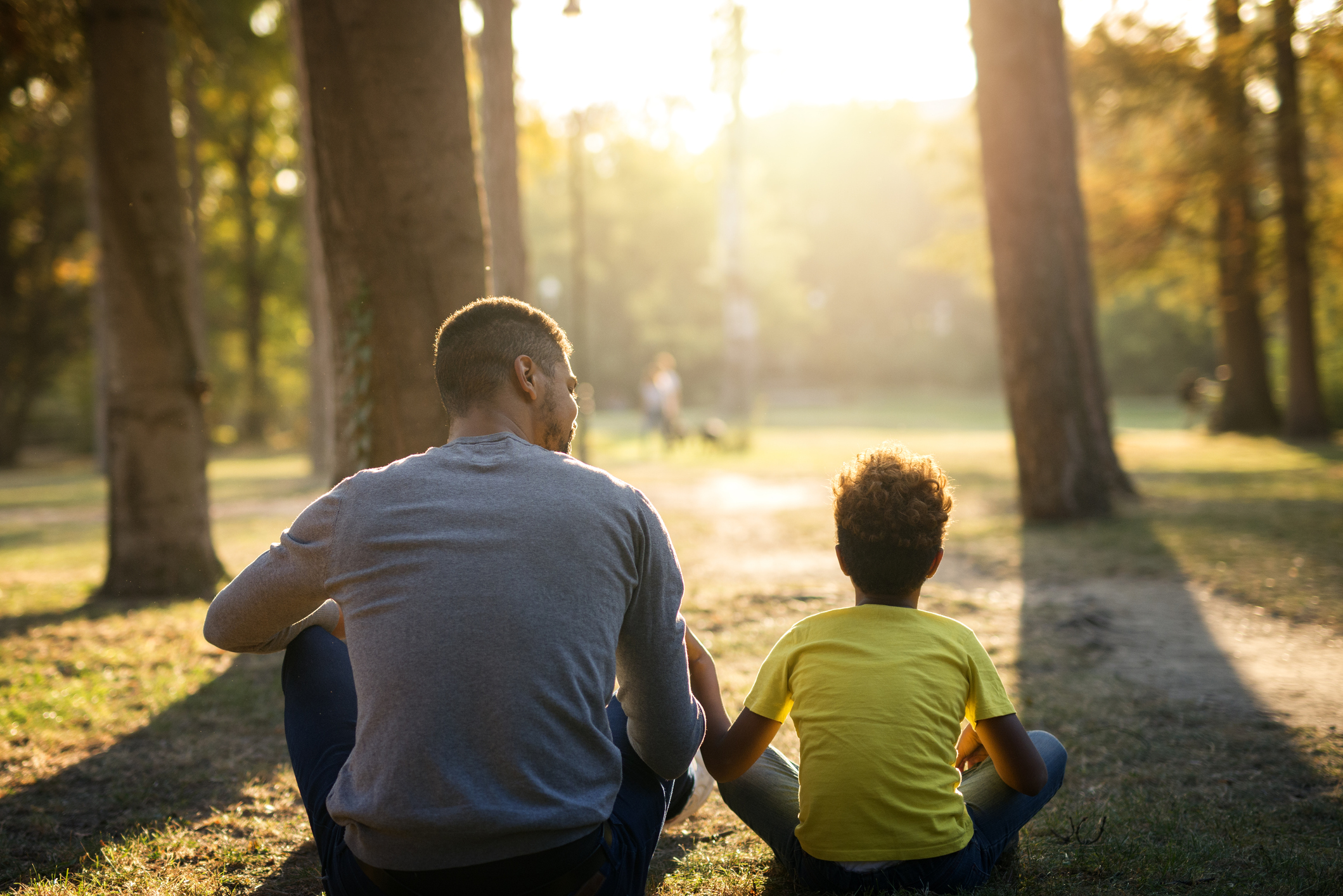 Father and daughter sitting on grass in park enjoying sunset together. People bonding.