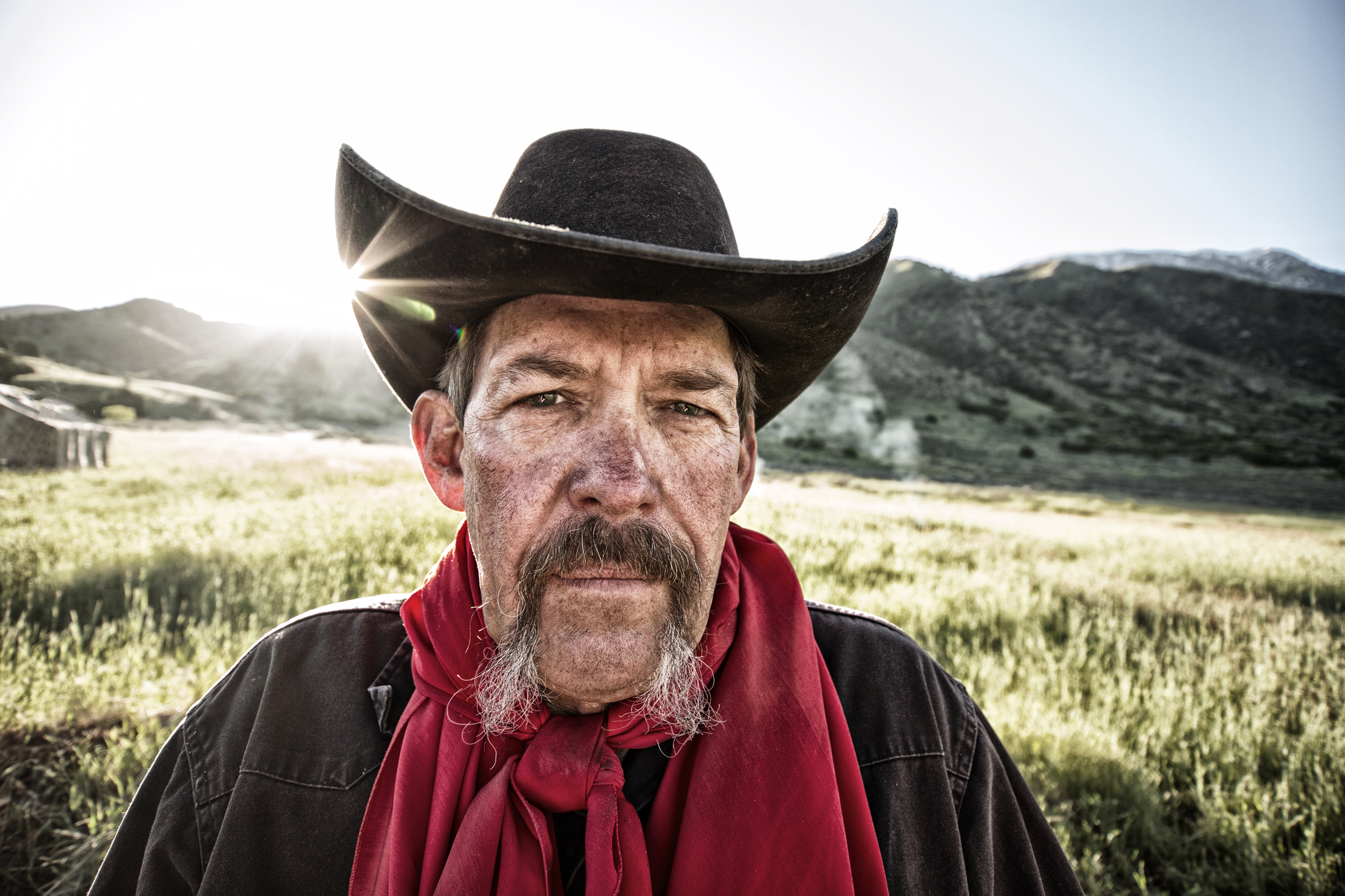 Mature cowboy  in a black hat looking like a western outlaw grimacing directly at the camera. Desaturated with added grunge.