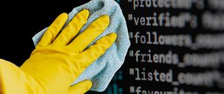 A hand in a yellow kitchen glove uses a light blue cloth to clean code off of a computer screen.