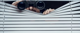 Man with binoculars looking through blinds.