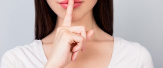 Shhh! Close up portrait of half face of young woman with finger showing hush silence sign, gesture and beauty concept, grey background, nice girl asking for silence