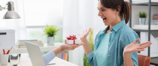 Cheerful young woman connecting to internet and receiving a present from a website, a male hand is coming out from the computer screen and giving her a gift box