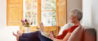 Shot of a mature woman relaxing on her sofa at home using a laptop
