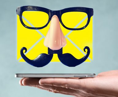 A yellow email icon with a false mustache and glasses floating over a cellphone resting on an open hand