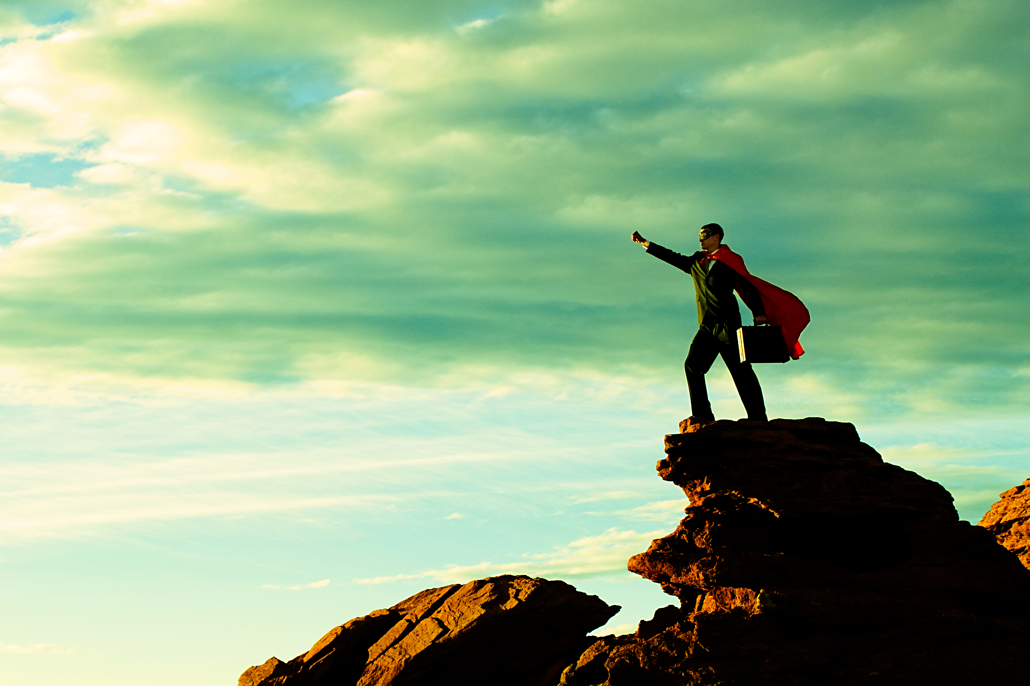 Business man in cape on top of mountain.