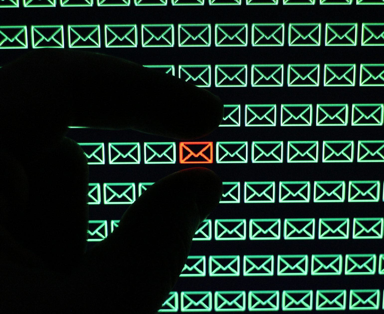 Shadow hand selecting red email icon from a field of green email icons.