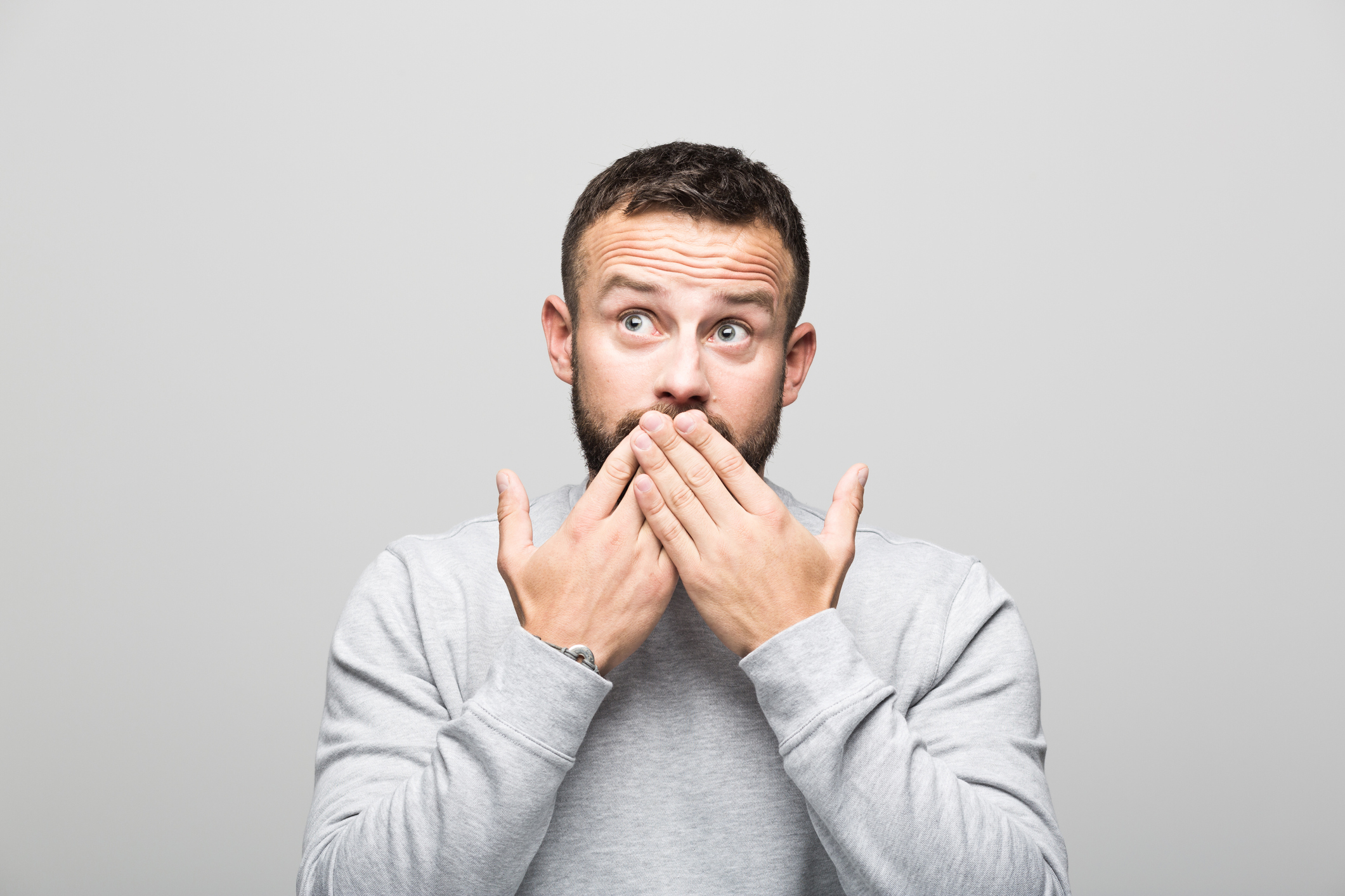 Portrait of shocked bearded young man looking up, grey background