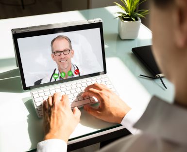 Businessman's hand videoconferencing with happy doctor on laptop