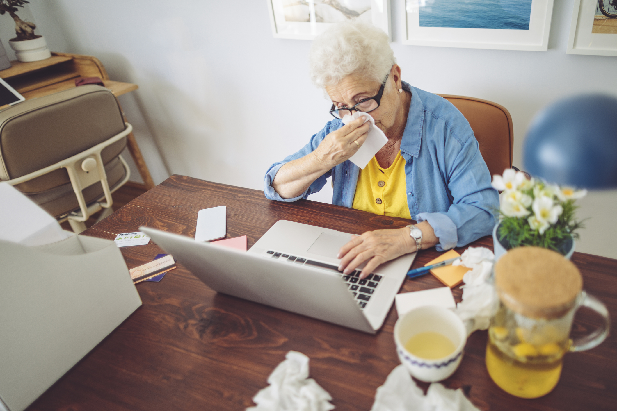 Senior woman at home on computer surrounded by used tissues.