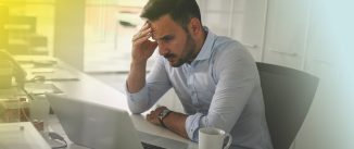 Frustrated man sitting in front of his computer with his hand on his head