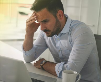 Frustrated man sitting in front of his computer with his hand on his head