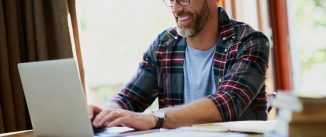 Man seated at computer at home happily typing.