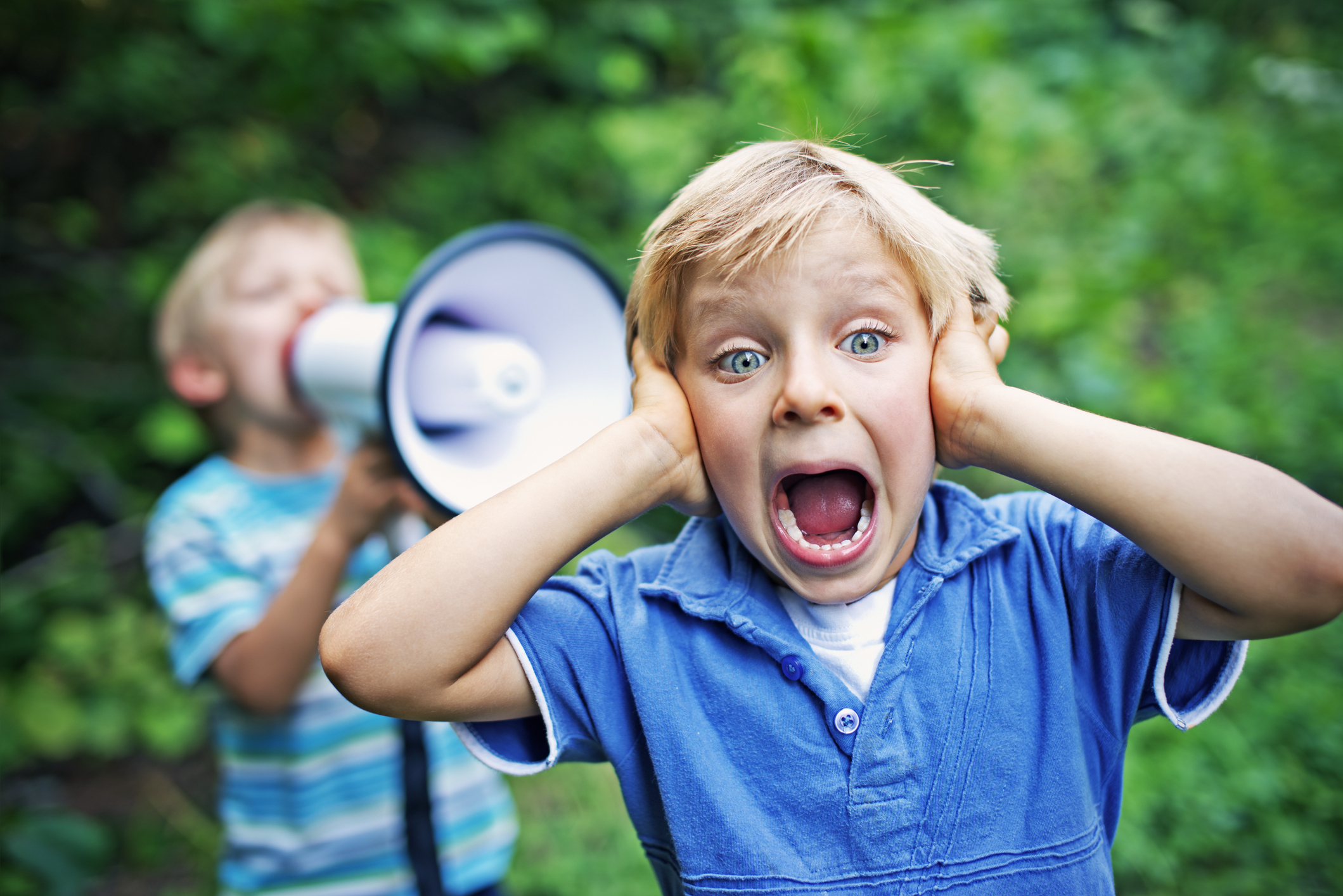 Little boy covering his ears while his brother is yelling on him with megaphone.