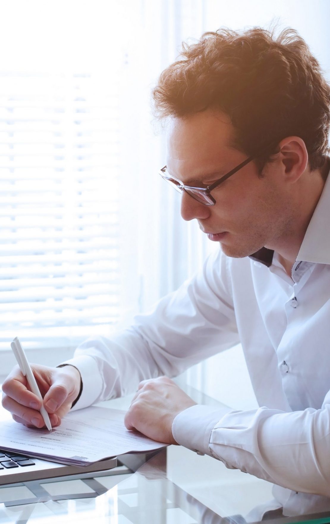 man writing while look at a laptop