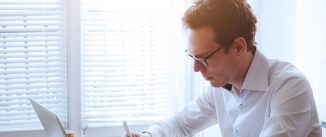 man writing while look at a laptop