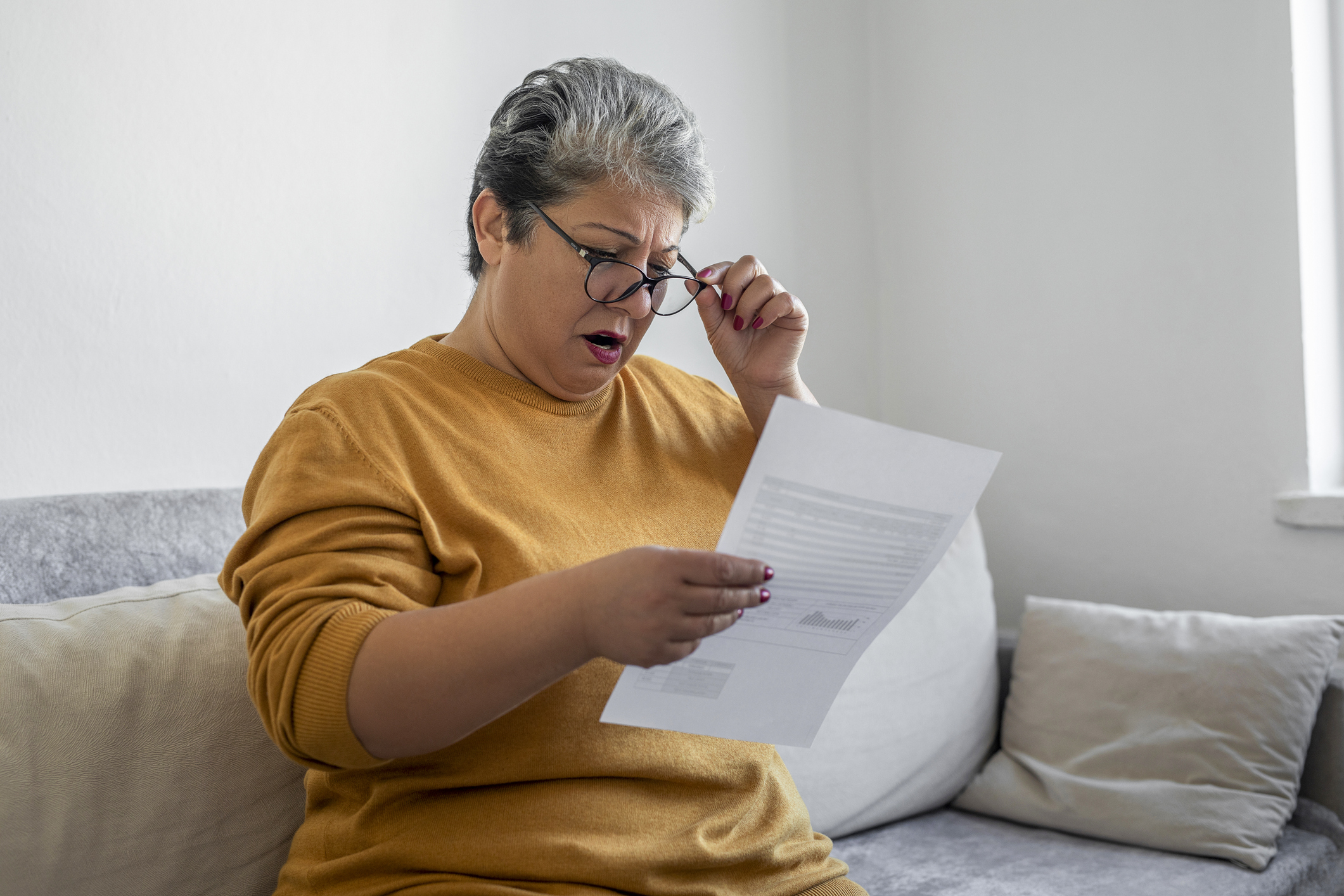 Woman sitting on a couch looking worried whle reading a letter