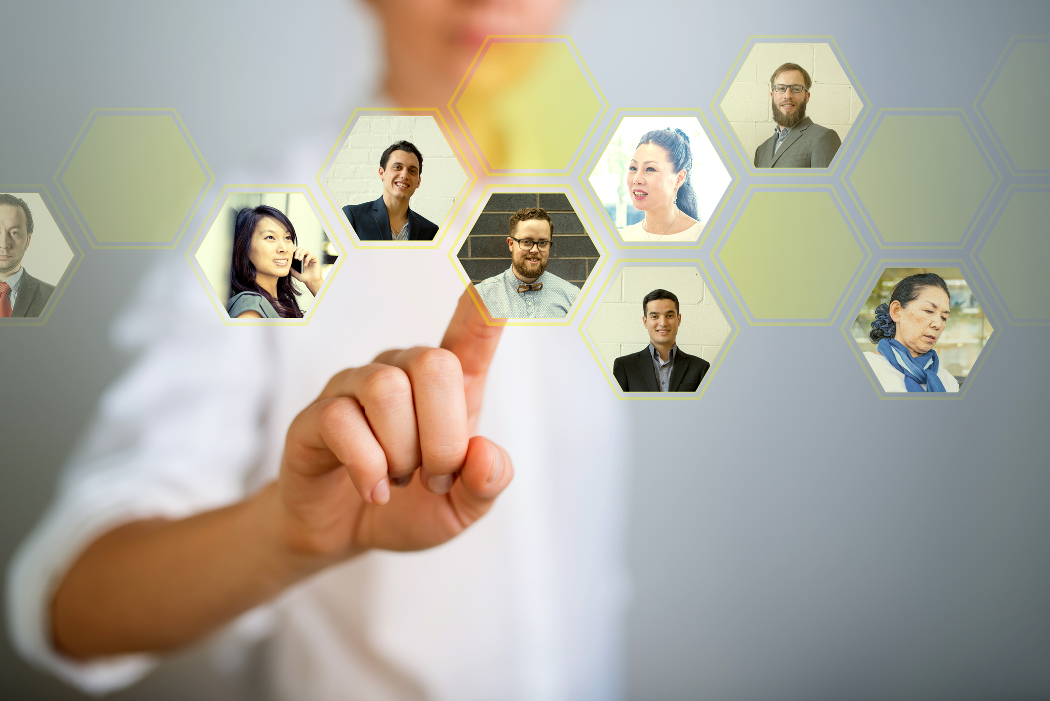 Young woman touching a grid of hexagon cells on a digital screenMany head shots on a wooden desk. A man is selecting a profile picture