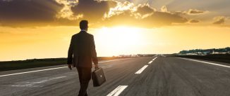 Entrepreneur, carrying a briefcase, walking on an empty highway at sunset.